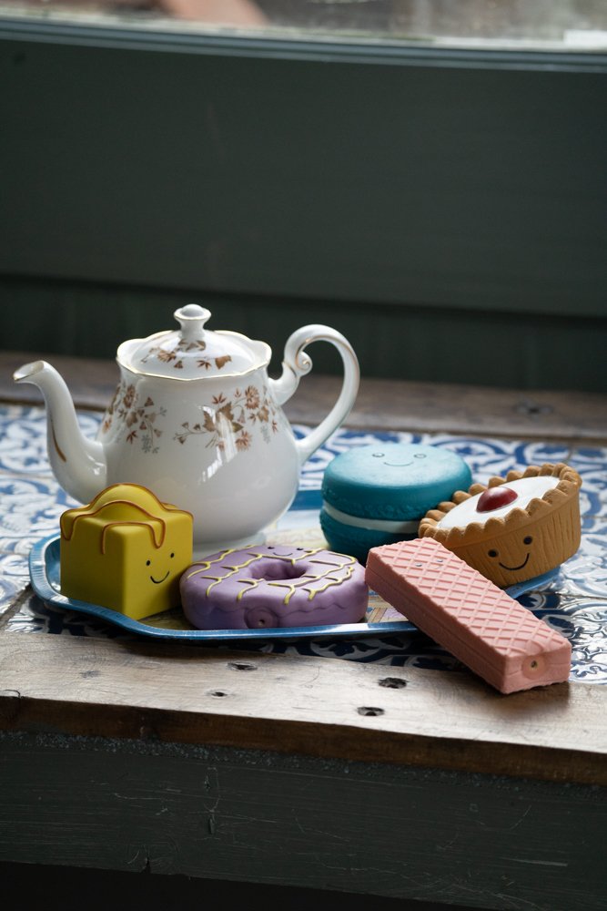 Teapot with colorful toys shaped like a wafer, donut, macaron, and pie on a tray. 