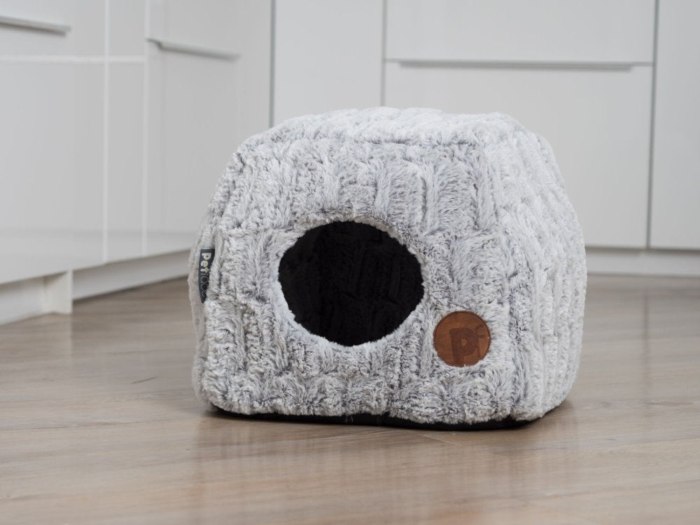 Textured pet bed with a round entrance on a wooden floor.