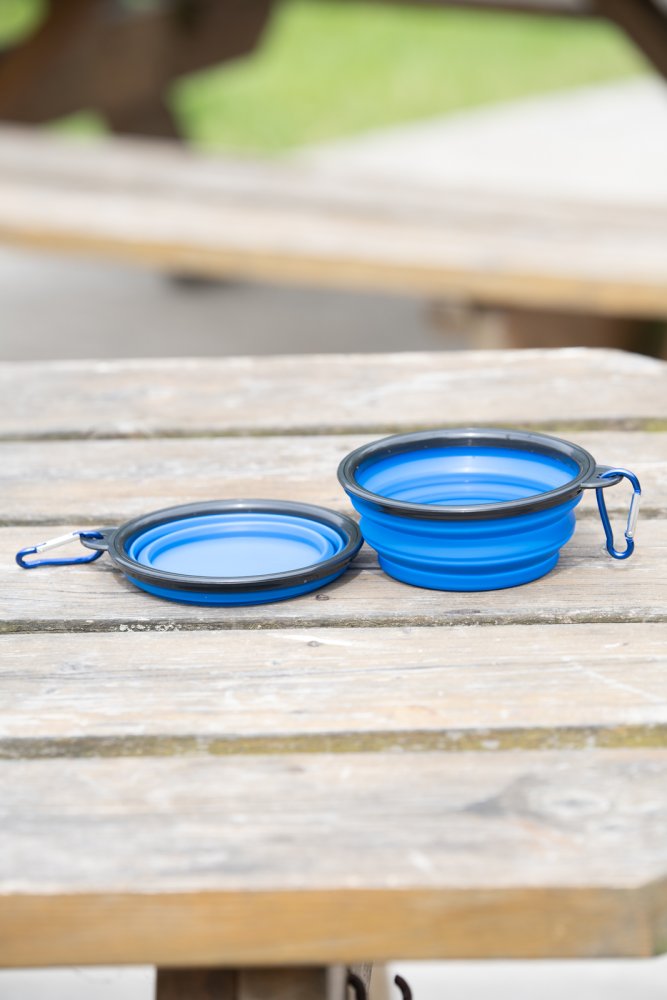 Two blue collapsible travel dog bowls outdoors on a wooden table