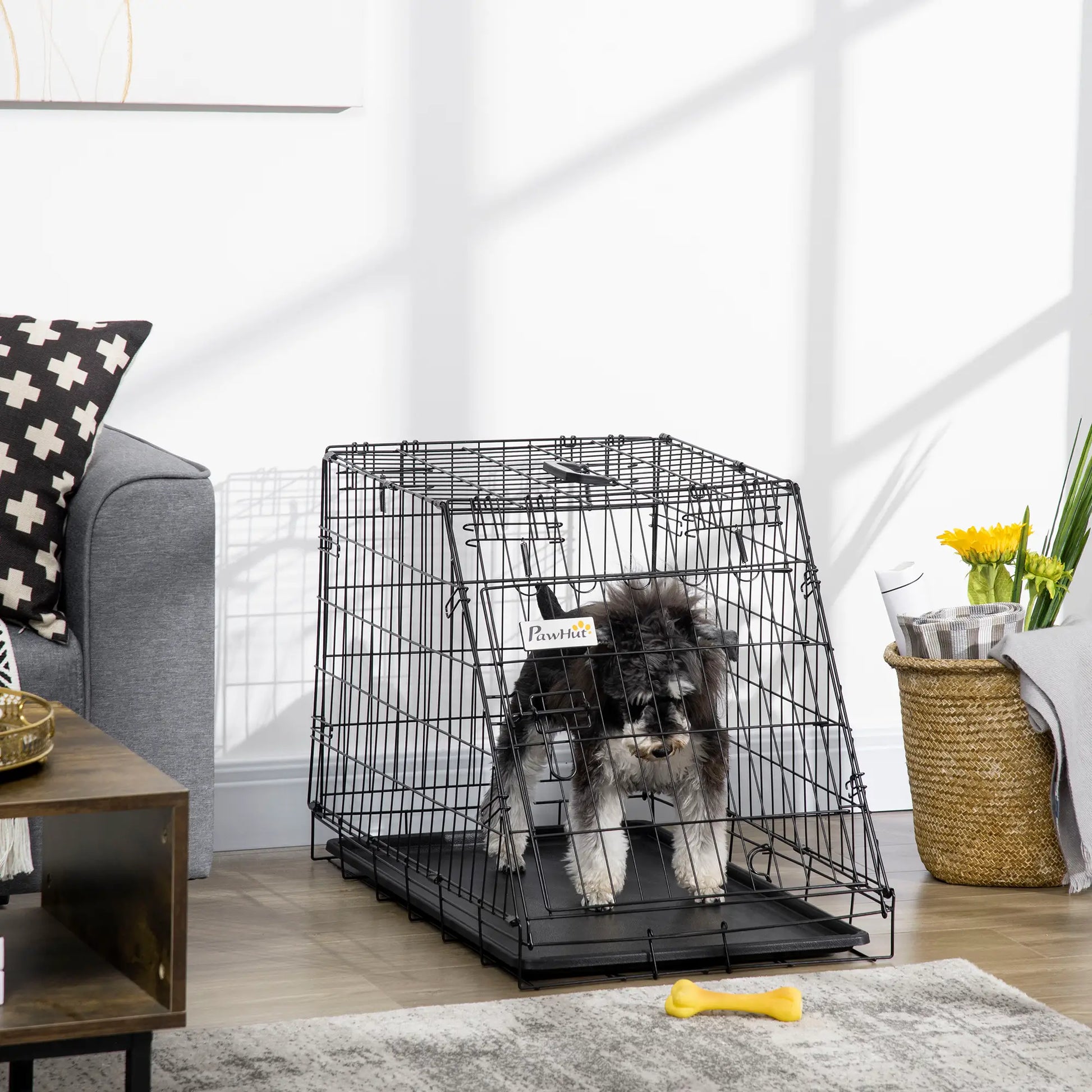 Dog inside a black crate in a living room setting with a couch, table, and decorative items.