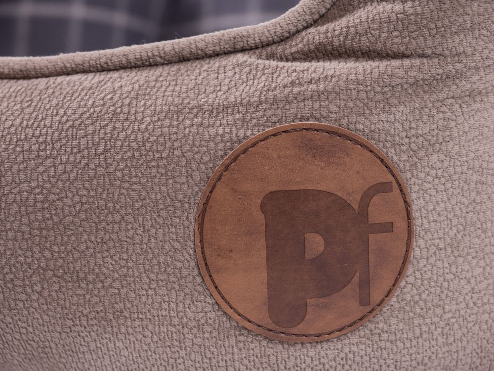 Close-up of a brown leather patch with 'PF' logo on a textured beige surface.